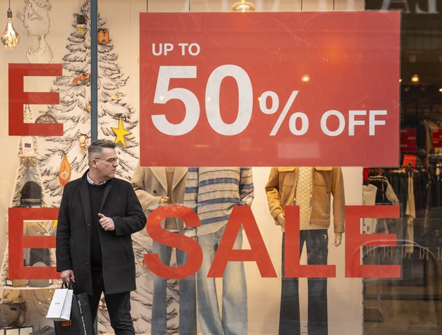 A man standing in front of a shop window, which has large signs on it saying 'Sale' and '50% off'