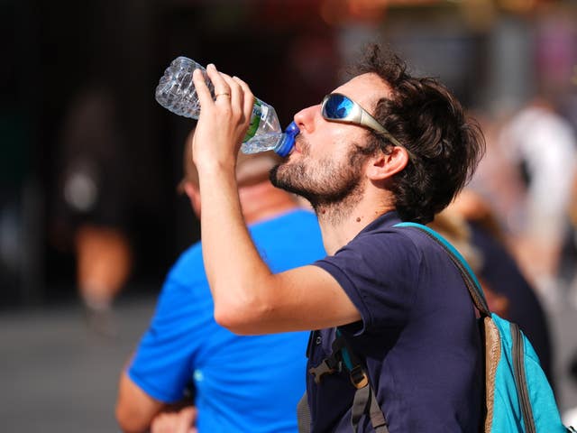 A person drinks a bottle of water while walking in Leicester Square, central London