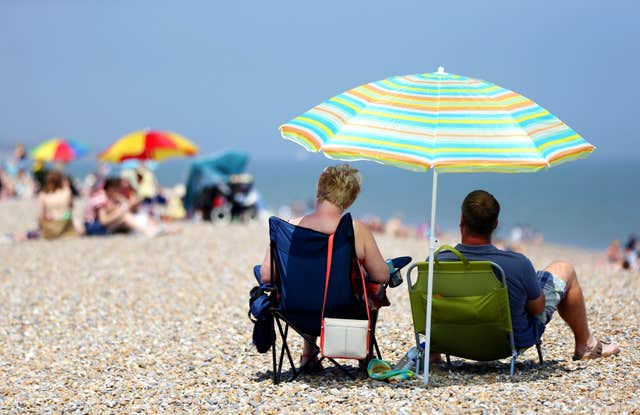 The back of two sunbathers in seats under a parasol on a stony beach