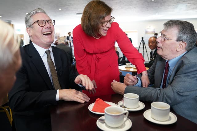 Labour Party leader Sir Keir Starmer laughing while sitting at a table with cups of coffee alongside Labour candidate Alex Baker during a visit to a veterans’ coffee morning at Aldershot Town Football Club