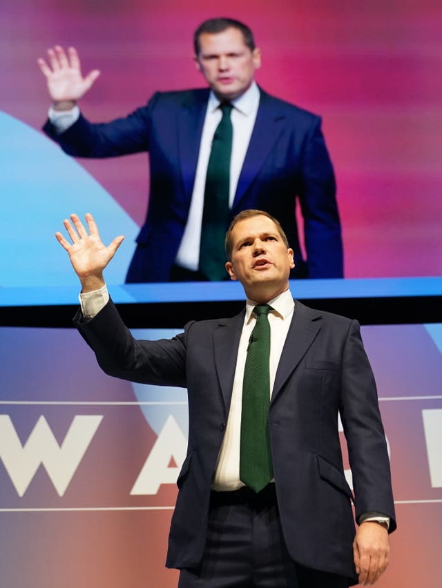 Robert Jenrick on stage with backdrop featuring his image 