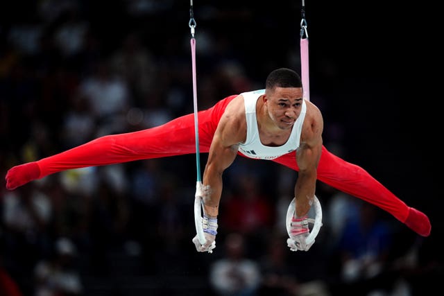 Joe Fraser, dressed in red bottoms and a white vest, on the gymnastic rings. 