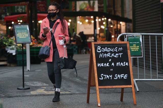 A shopper passes a coronavirus advice sign at Borough Market, London, which became the first outdoor space in the UK to legally enforce the wearing of face masks for all customers and stallholders