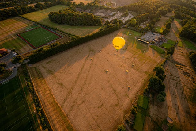 A hot air balloon flies over a browning and parched golf driving range early in the morning