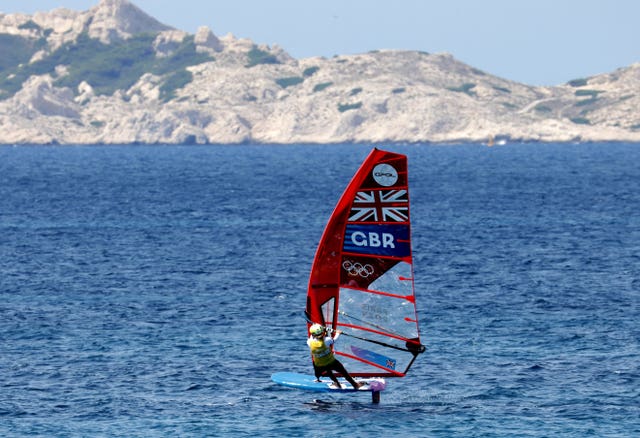 Great Britain’s Emma Wilson on her windsurfer with a GBR logo and mountains in the background. 