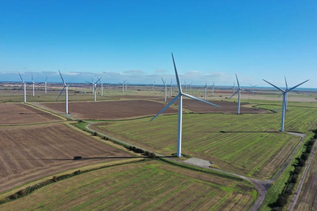 Numerous wind farms on brown and green fields, beneath blue skies