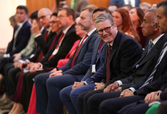 Sir Keir Starmer sitting forward and smiling while sitting in a row of people in business dress