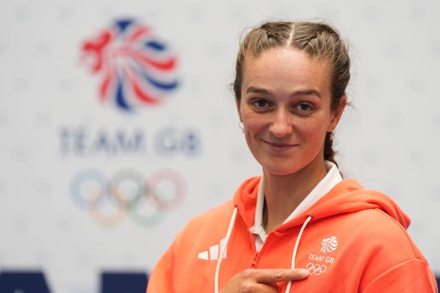 Mallory Franklin, wearing an orange hoodie, points at her Team GB badge.