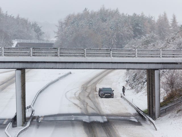 A person stands next to his vehicle on an empty snow-covered M9 motorway near Stirling