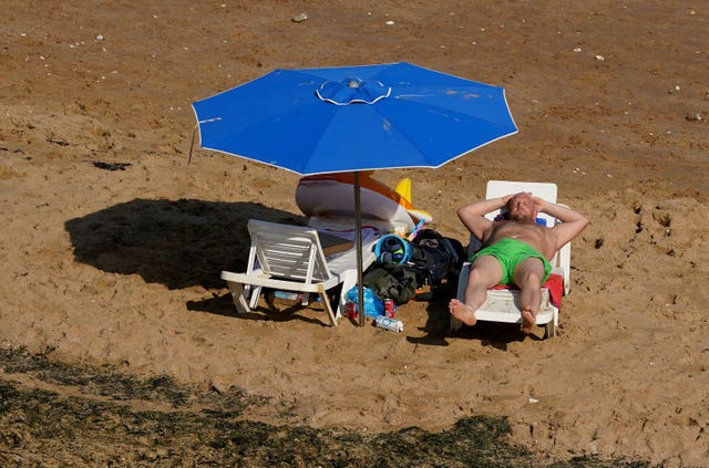 A man lies on a sun lounger on sand under a parasol