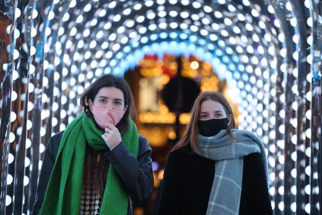 Two women wearing facemasks walking through a tunnel of lights