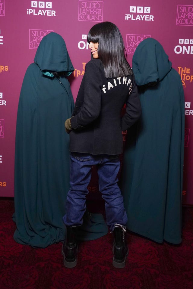 Claudia Winkleman, standing in the middle of two hooded figures, wears a black jacket with the word faithful written on the back