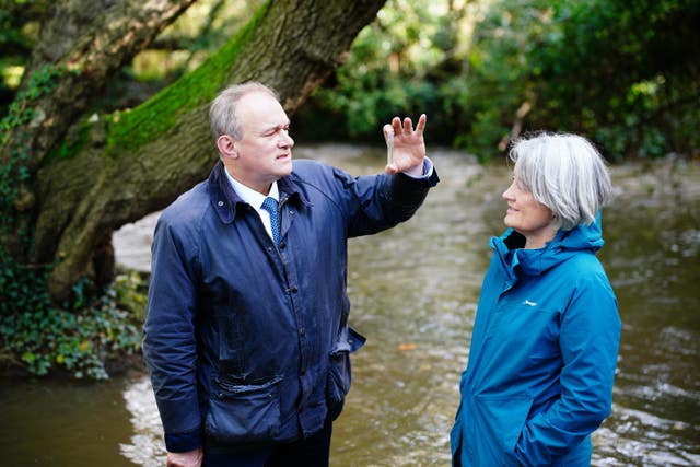 Sir Ed Davey speaks to a woman while standing in a river
