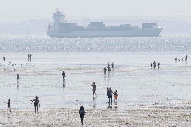 People paddle in the sea with a ship in the background