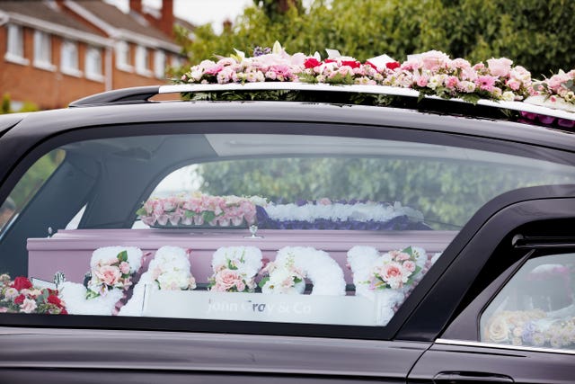 A pink coffin in the back of a hearse, surrounded by floral tributes