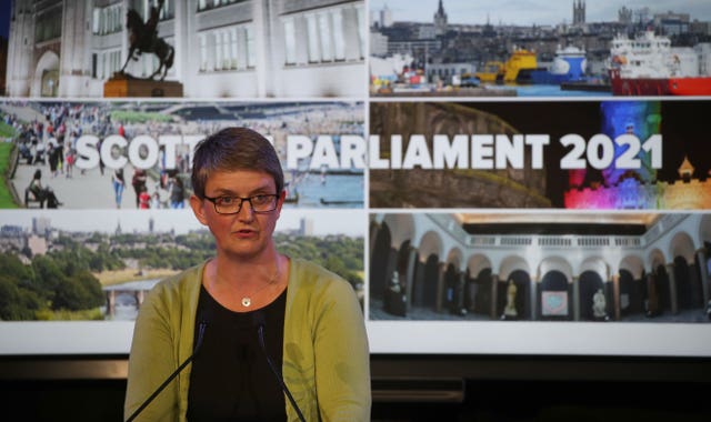 Maggie Chapman speaking from a podium with election posters behind her