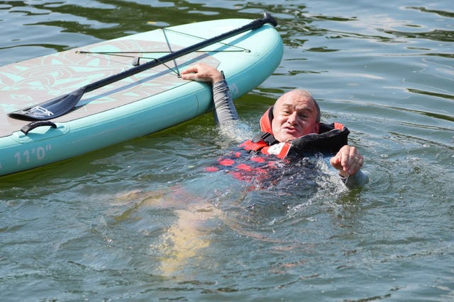 Liberal Democrat leader Sir Ed Davey in the water, wearing a life jacket, having tumbled off a turquoise paddleboard