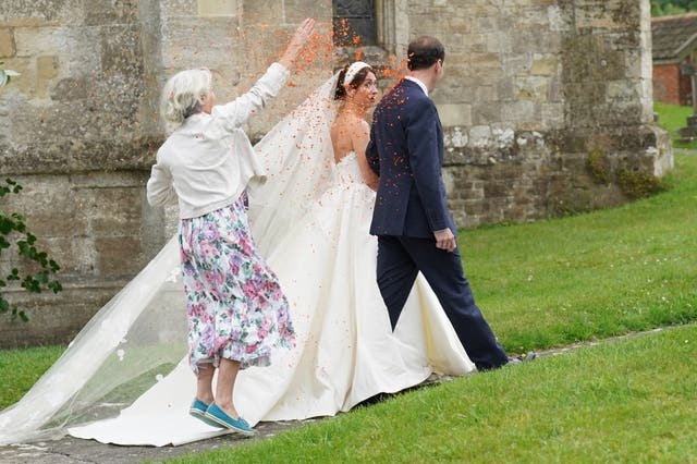 A woman throws orange confetti over the newly married couple as they leave St Mary’s Church in Bruton (Stefan Rousseau/PA)