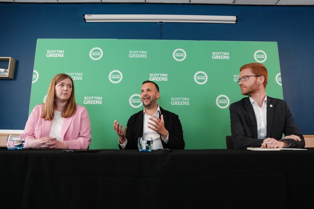 Zack Polanski speaking in front of Scottish Green signage, flanked by Gillian Mackay and Ross Greer