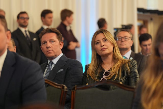 Property developer Nick Candy and his wife Holly Valance sit together listening to a speech surrounded by an audience sitting and standing