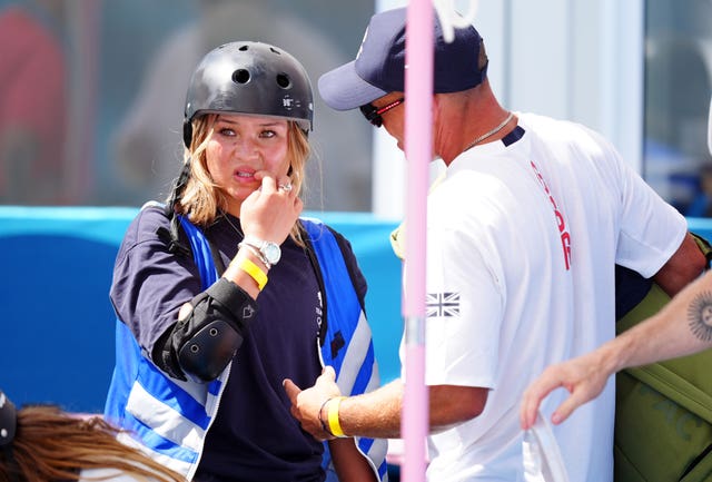 Sky Brown scratches her face while her coach talks to her. 