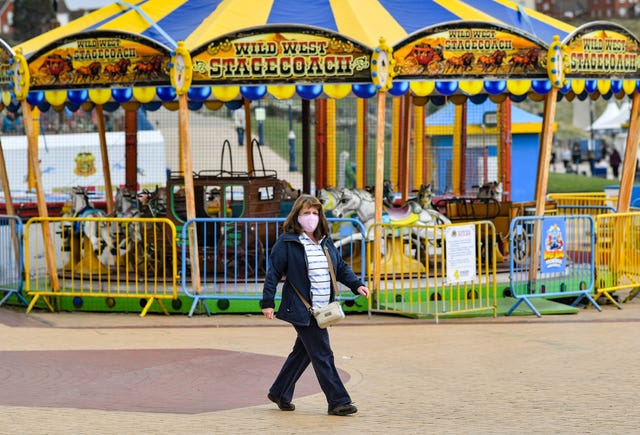 A woman walks past closed fairground rides on the seafront at Barry Island in the Vale of Glamorgan (Ben Birchall/PA)