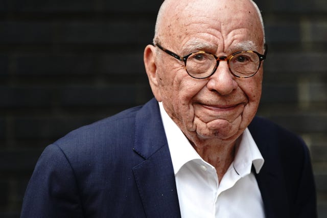 Rupert Murdoch smiling wearing glasses, a white shirt and navy jacket
