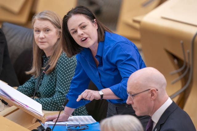 Kate Forbes, in blue shirt, standing while speaking in Parliament