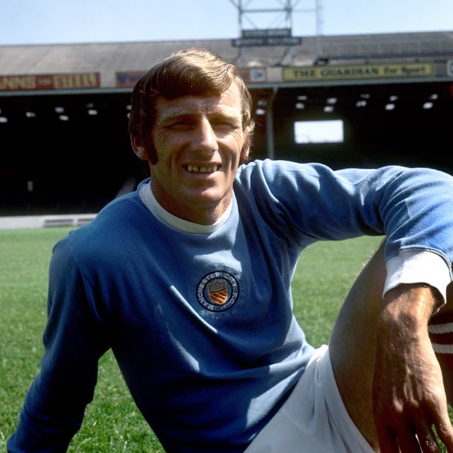 Tony Book, wearing his Manchester City kit, sits on the grass at Maine Road