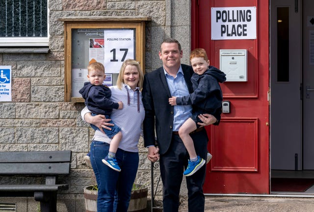 Douglas Ross holds his son in his arms and holds hands with his wife, who is holding their other son, outside a polling place