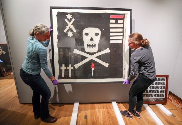 Exhibition staff hang a Jolly Roger from HMS Unison 