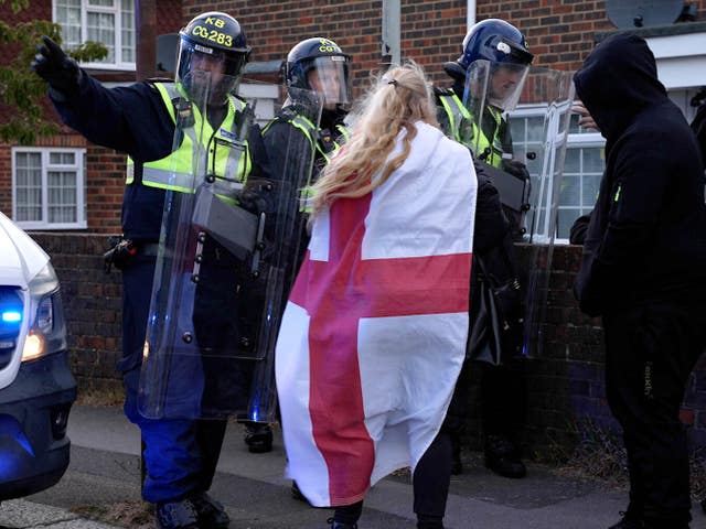 A woman draped in a St George's Cross flag, centre, and a figure in a hooded top, right, speaking to three police officers wearing riot gear and shields