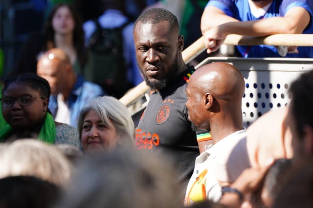 Stormzy watching the multi-faith and wreath laying ceremony on a big screen at the base of Grenfell Tower 