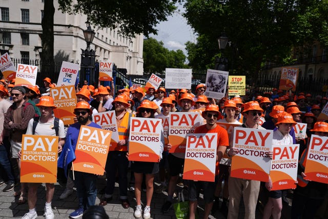 A large group of junior doctors on strike, wearing orange BMA hats and holding placards reading 'Pay restoration for doctors'
