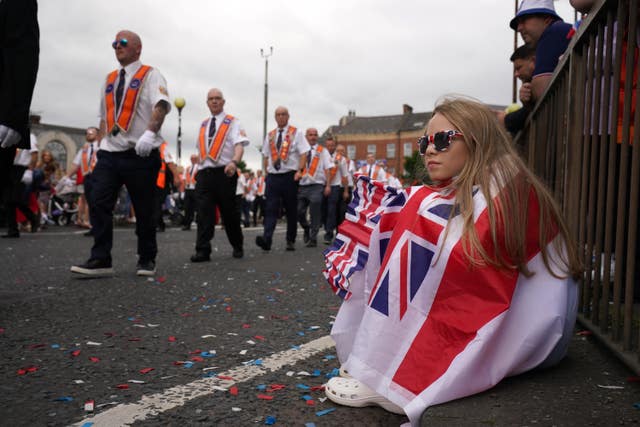 A girl sitting on the ground wrapped in a red and white flag and holding a Union flag