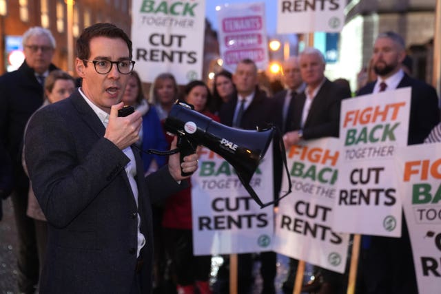 Ciaran Ahern in the foreground speaking into a megaphone while standing in front of protesters holding placards