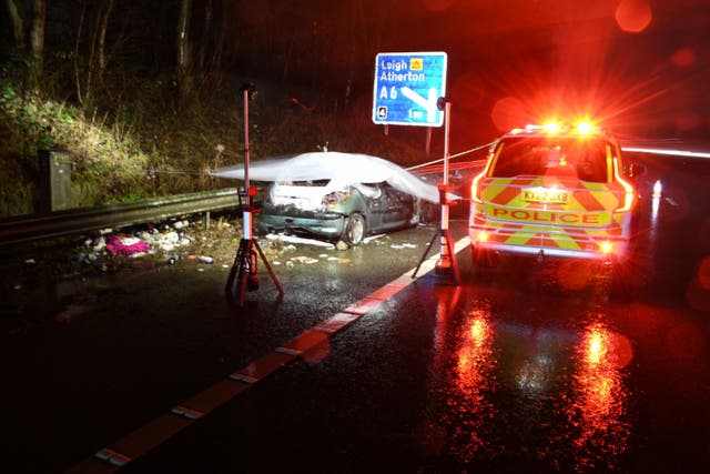 Police car with flashing lights parked next to a burnt out car on a road