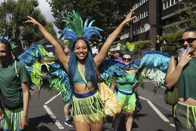 A woman with blue hair and a feathered headdress waves her hands in the air 