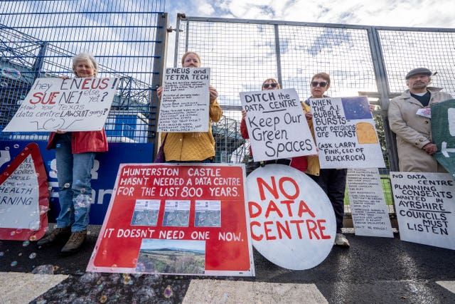 Protesters holding placards outside a large fence