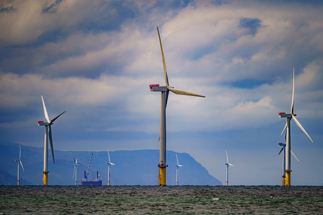 A view of offshore wind turbines, with the coastline in the background