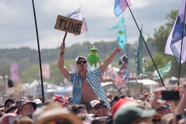 A man in a striped shirt holding a sign that says "tune" with Kermit the Frog doll held beside him