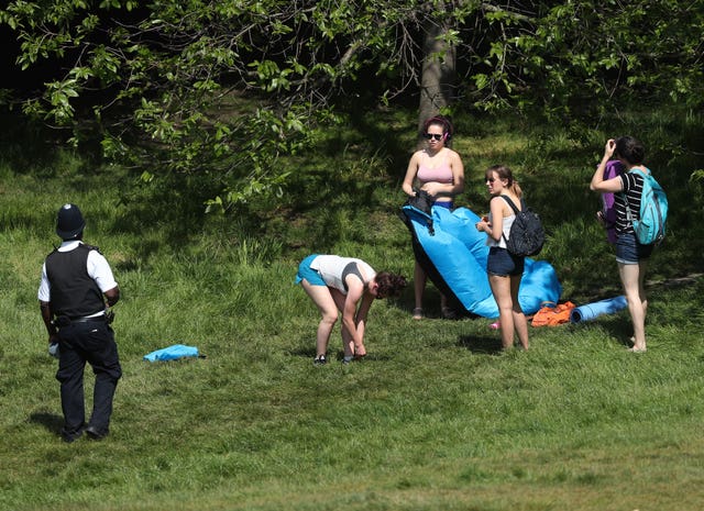 A police officer moves sunbathers on in Greenwich Park, London