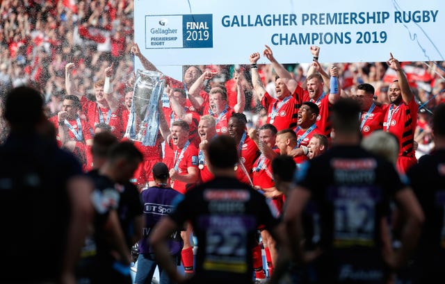 Saracens lift the 2019 Premiership trophy while Exeter players watch on