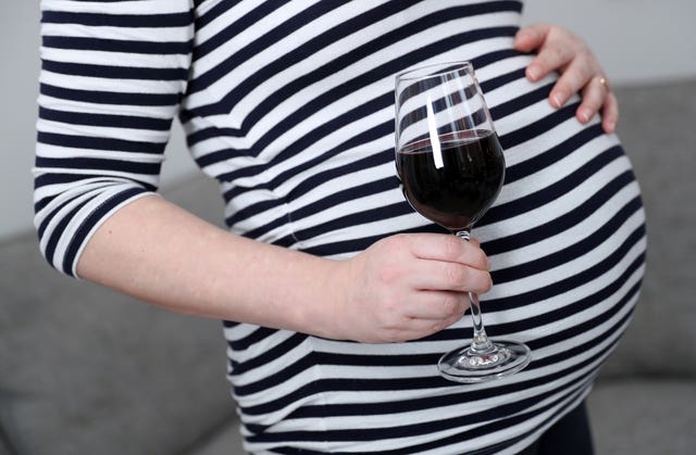 A pregnant woman holds a glass of red wine in her hand whilst holding her stomach (Andrew Matthews/PA)