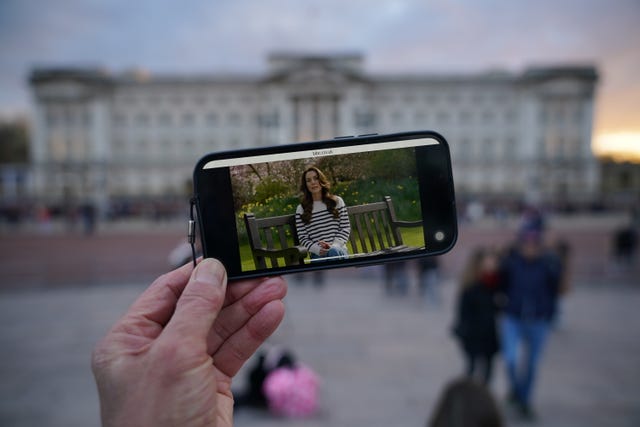 A person watches Kate's announcement on a smartphone outside Buckingham Palace