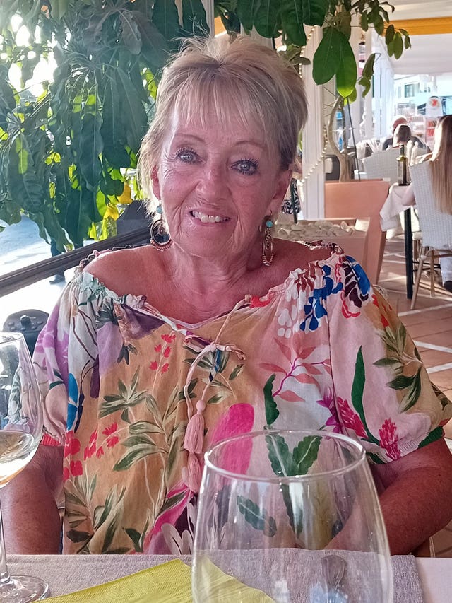 Head and shoulders of an older woman wearing a brightly coloured top 