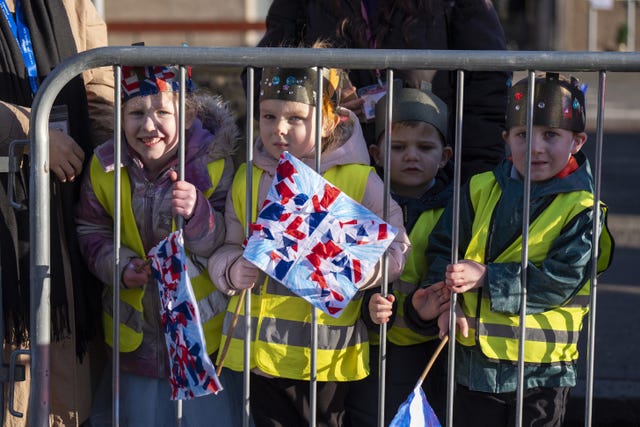 Four small children in hi-viz vests, viewed through fencing