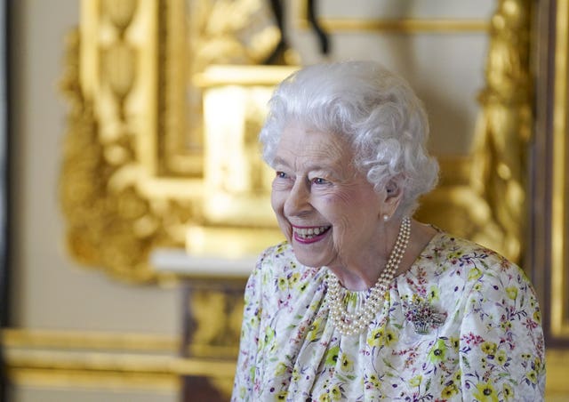 The Queen smiles as she stands near an ornate mirror in a royal residence