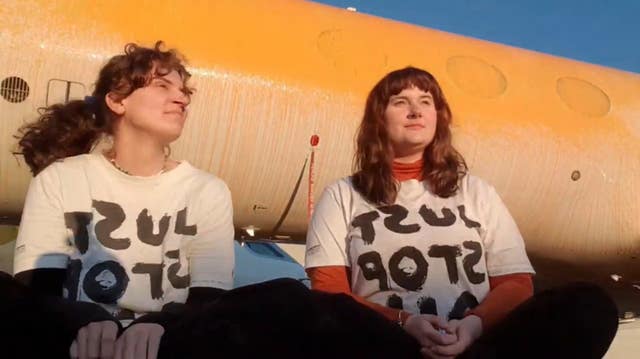 Jennifer Kowalski (left), and Cole Macdonald sit on the ground after they sprayed orange paint over parked private jets at London Stansted Airport