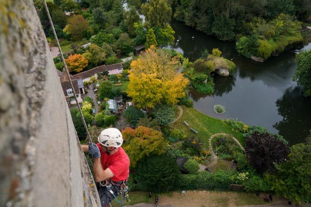 Person in red T-shirt and white hard hat seen from above abseiling down a castle wall